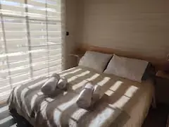 Cama matrimonial de Cabaña Magia iluminada por el sol patagónico con revestimiento cálido en madera