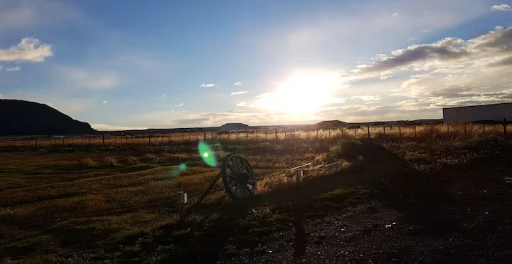 Atardecer dorado en la estepa patagónica con rueda de carreta tradicional y cerros de Puerto Natales al fondo